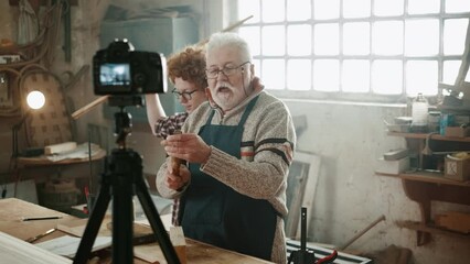 Elderly youtube teacher explaining on camera recording a video, how to using wood for carpentry online course. Online teaching of carpentry