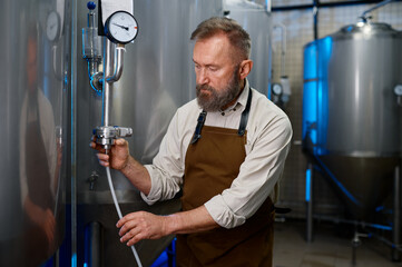 Adult bearded man in workshop of modern industrial brewery