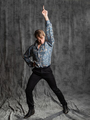 Stylish elegant young man in a blue silk shirt posing in the studio on a gray fabric background. superstar pose