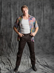 A relaxed dude in a colorful shirt and a white T-shirt, posing in the studio on a gray background