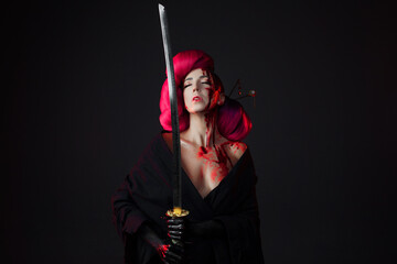 A fighting geisha with a katana, splashes blood on her face. Halloween image. young multiethnic woman in a bright Asian costume. voluminous hairstyle with scarlet hair and decorative hairpins