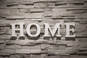 Auf einer mit schmalen Steinen bedeckten Mauer steht das Wort "Home" geschrieben.
