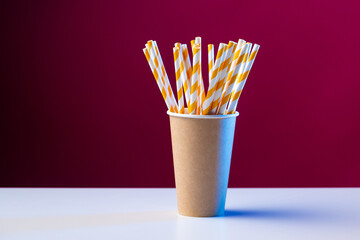 Disposable cardboard biodegradable cup on a white table with a straw against a red background.