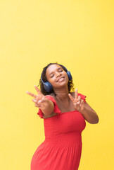 Black woman happy and dancing while listening to music on wireless headset with yellow background.