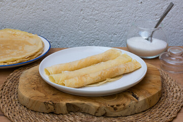 Dulce típico de carnaval en Galicia (filloas). Tortitas o crepes hechos en sartén, plato blanco sobre madera, fondo blanco. - obrazy, fototapety, plakaty