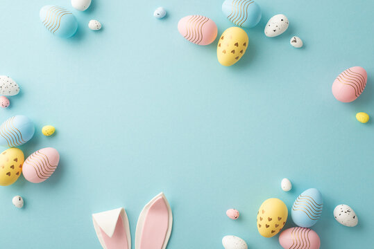Naklejka Easter party concept. Top view photo of easter bunny ears white pink blue and yellow eggs on isolated pastel blue background with copyspace in the middle