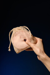 In hand is a handbag with a cotton reusable pink make-up remover pad in a mesh fabric bag, on a...