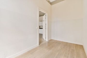 an empty room with white walls and wood flooring on the right side, there is a door leading to...