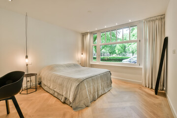 a bedroom with a bed, chair and desk in front of a large window looking out to the street outside