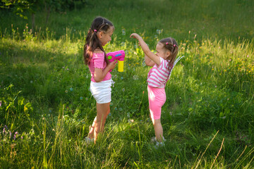 Preschool girls are having fun playing and blowing soap bubbles from a gun.