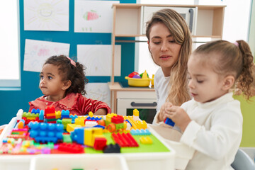 Fototapeta premium Teacher with girls playing with construction blocks sitting on table at kindergarten