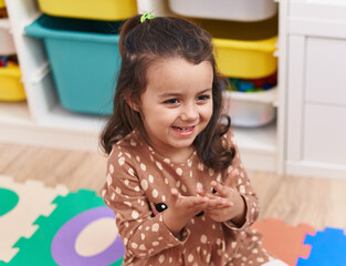 Adorable hispanic girl smiling confident sitting on floor at kindergarten