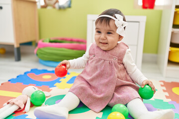 Adorable hispanic baby playing with balls sitting on floor at kindergarten