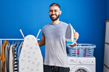 Middle east man with beard holding electric iron winking looking at the camera with sexy...