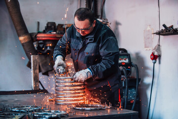 Locksmith in special clothes and goggles works in production. Metal processing with angle grinder....