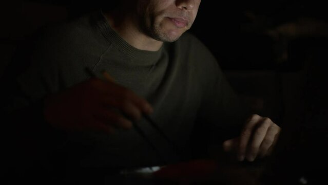 Man eating sushi as he works late on his laptop in the dark