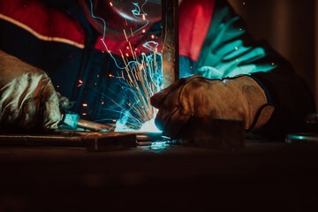 Close up welder in protective uniform and mask welding metal pipe on the industrial table with...