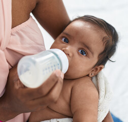 African american baby sucking feeding bottle at bedroom