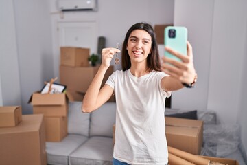 Young beautiful hispanic woman having video call holding key at new home