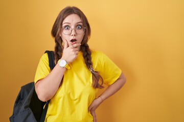 Young caucasian woman wearing student backpack over yellow background looking fascinated with...