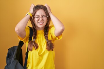 Young caucasian woman wearing student backpack over yellow background suffering from headache...