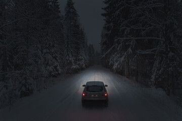 Driving a car on a forest snowy road at night. Headlights light the way