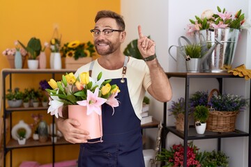 Middle age man with beard working at florist shop holding plant surprised with an idea or question pointing finger with happy face, number one
