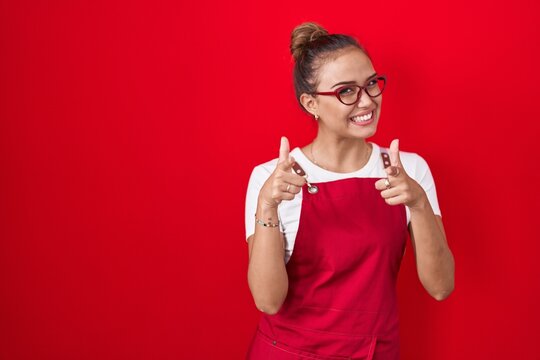 Young hispanic woman wearing waitress apron over red background pointing fingers to camera with happy and funny face. good energy and vibes.