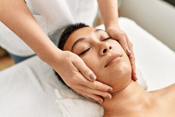 Obraz na płótnie Canvas Young hispanic woman having facial massage at beauty center