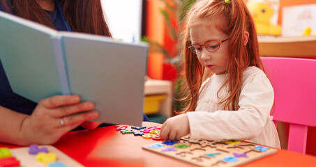 Adorable redhead girl playing with maths puzzle game sitting on table at kindergarten