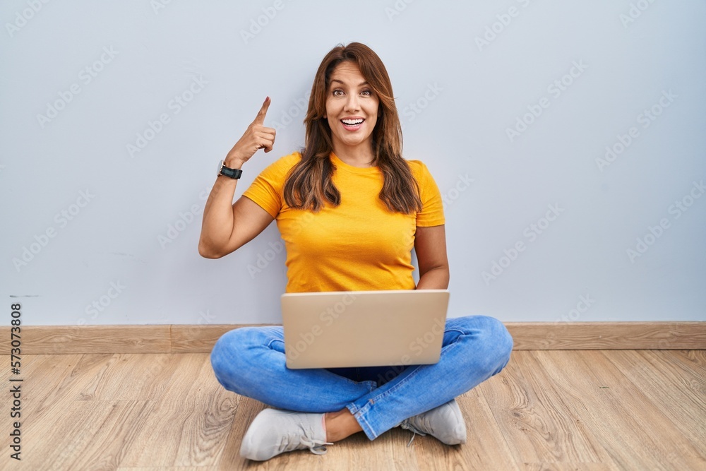 Sticker hispanic woman using laptop sitting on the floor at home smiling amazed and surprised and pointing u