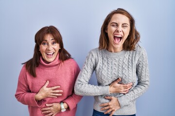 Mother and daughter standing over blue background smiling and laughing hard out loud because funny...