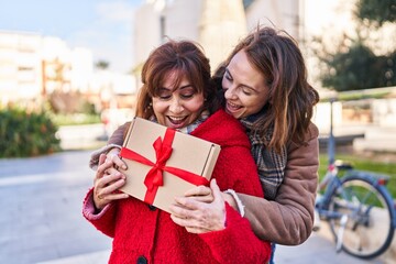 Two women mother and daughter hugging each other surprise with gift at park