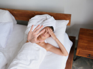A woman lies on a bed in the morning on a pillow under a blanket in the bedroom after a shower in a towel, feeling unwell cold and headache from a virus, health problems, hangover, female pain