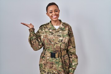 Beautiful african american woman wearing camouflage army uniform smiling cheerful presenting and pointing with palm of hand looking at the camera.