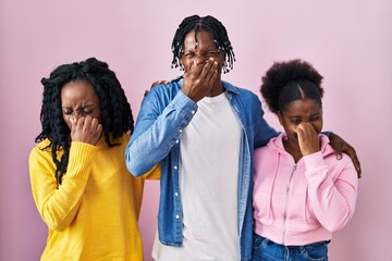 Group of three young black people standing together over pink background smelling something stinky...