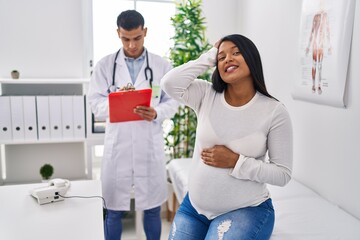 Young hispanic mother expecting a baby at the doctor stressed and frustrated with hand on head, surprised and angry face