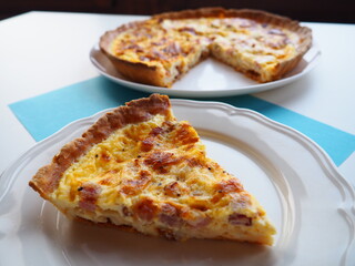 Homemade traditional french Quiche Lorraine, real recipe, slice on a plate, white and blue background