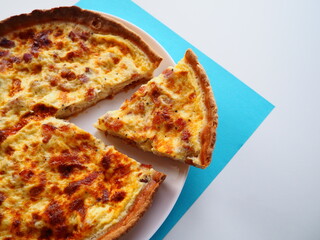Homemade traditional french Quiche Lorraine, real recipe, a slice cut apart, white and blue background, space for text