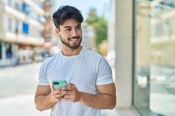 Young hispanic man smiling confident using smartphone at street