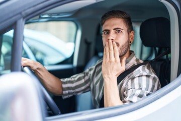 Hispanic man with beard driving car covering mouth with hand, shocked and afraid for mistake....
