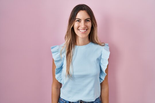 Young hispanic woman standing over pink background with a happy and cool smile on face. lucky person.