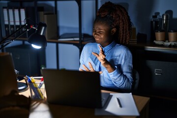 African woman working at the office at night disgusted expression, displeased and fearful doing disgust face because aversion reaction. with hands raised