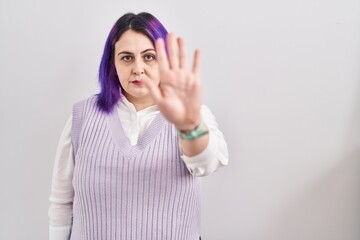 Plus size woman wit purple hair standing over white background doing stop sing with palm of the hand. warning expression with negative and serious gesture on the face.
