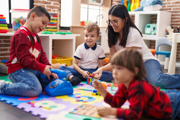 Teacher with group of boys playing with toys sitting on floor at kindergarten