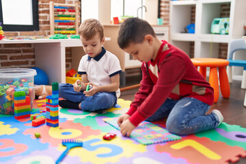 Two kids playing with construction blocks and maths puzzle game sitting on floor at kindergarten