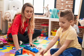 Teacher and toddler playing with cars toy sitting on floor at kindergarten