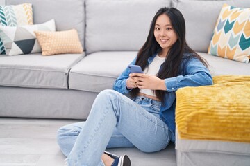 Young chinese woman using smartphone sitting on floor at home