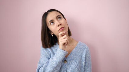 Young beautiful hispanic woman standing with doubt expression over isolated pink background