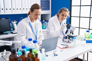 Two women scientists using microscope and laptop at laboratory